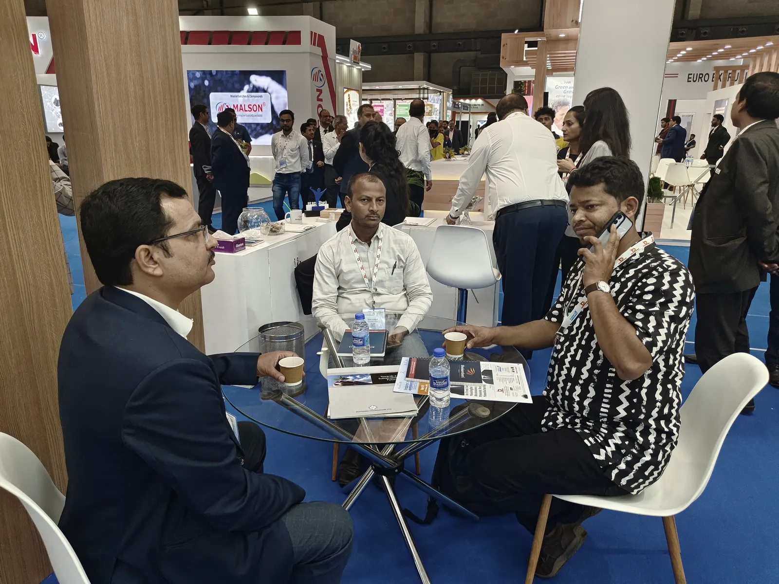 Visitors in conversation at the stand's glass table, Indplas 2025